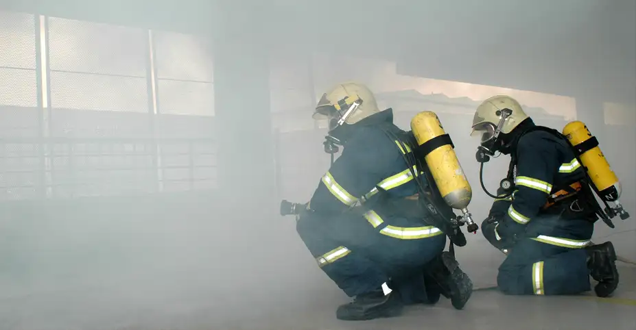 Two firefighters fully equipped knelt down in a cloud of smoke